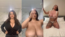 JuicyJade fazendo um strip enquanto exibe seus peitões e saborosos