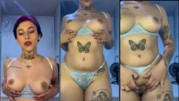 Uma garota nova, com tatuagens, ousada, tirando a roupa íntima e ficando nua